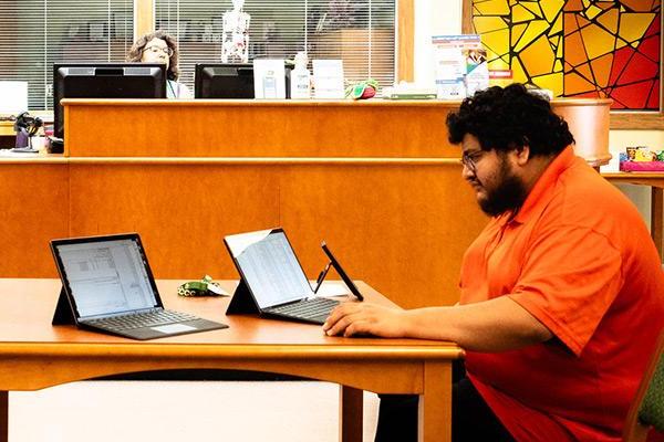 Student sitting at library table interacting with a few different electronic devices  